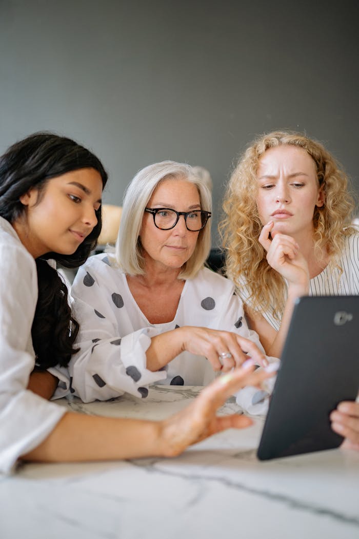 A diverse group of women discussing and interacting with a tablet during a collaborative meeting.